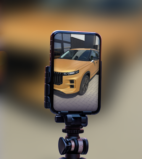 A close-up shot of a smartphone screen showing a golden JAECOO 7 car parked outdoors, with the phone mounted on a tripod.
